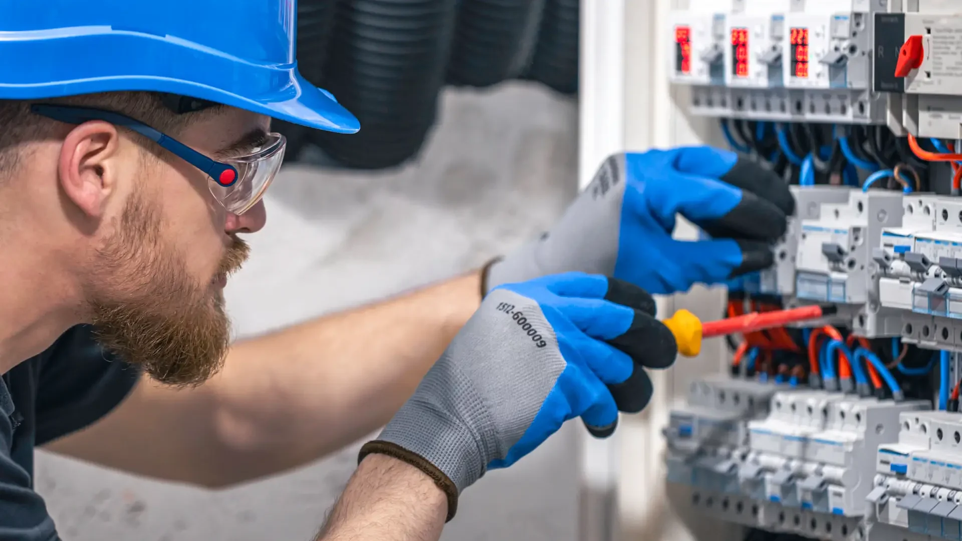 A male electrician works in a switchboard with an electrical connecting cable.